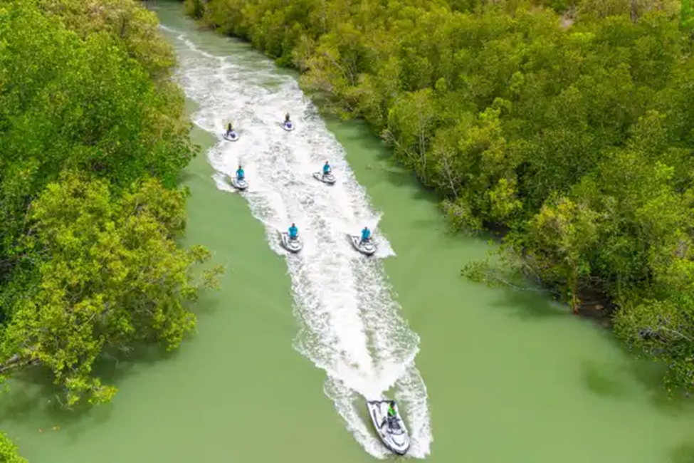 Aerial view of multiple jet skis riding in a guided formation through green water near Phuket.