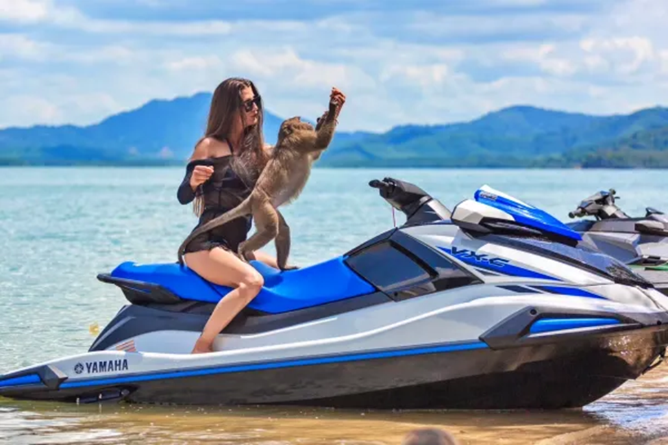 Traveler sitting on a blue jet ski during a beach stop with calm sea and mountains in the background.